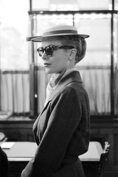 a woman wearing a hat and sunglasses standing in front of a table with papers on it