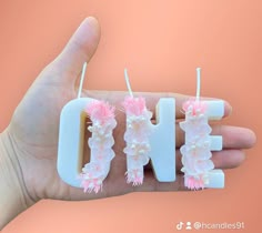 a hand holding three small candles that spell out the word love with flowers on them