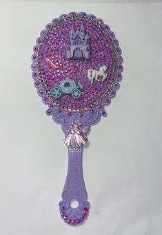 a purple hair brush with beads on it and a castle in the middle, sitting on a white surface