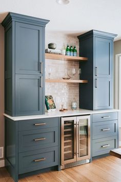 an empty kitchen with blue cabinets and white counter tops is pictured in this image, there are wine glasses on the shelves