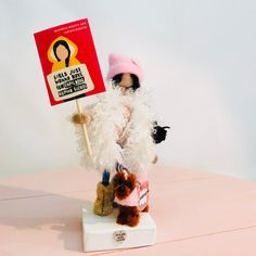 a small stuffed animal holding a sign on top of a white table next to a pink wall