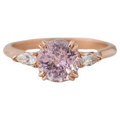 a pink diamond ring with two white diamonds on the band and an oval shaped center stone