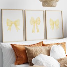 three framed pictures hang on the wall above a bed with white sheets and gold pillows