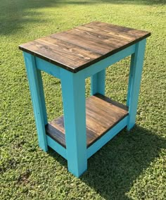 a small wooden table sitting on top of a green grass covered field with trees in the background