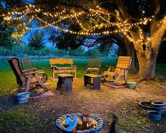 a group of wooden chairs sitting under a tree next to a fire pit with lights on it