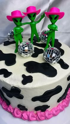 the cake is decorated with black and white cow print, pink trimmings, and green figures