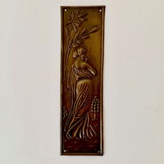 a metal plaque with a woman holding a plant on it's side, in the shape of a rectangle