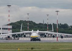 an airplane that is sitting on the runway in front of some trees and buildings,