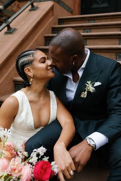 a bride and groom are sitting on the steps kissing each other with flowers in front of them