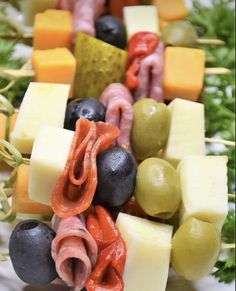 an assortment of cheeses, olives, and meat skewers on a platter