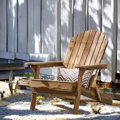 a wooden chair sitting on top of a sandy ground next to a white fence and flowers