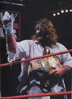 a man in a wrestling ring with his hand up to the sky and wearing a mask