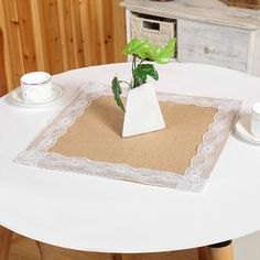 a white table topped with a vase filled with a plant next to a cup and saucer