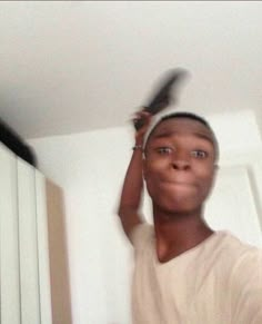 a young man holding a pair of scissors up to his head while standing in front of a mirror