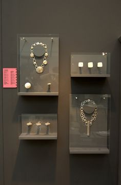 two glass shelves with necklaces and bracelets on them in front of a gray wall