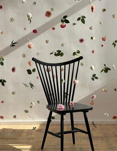 a black chair sitting on top of a hard wood floor next to a wall covered in flowers