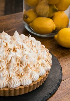 a lemon meringue pie sitting on top of a wooden table next to some lemons