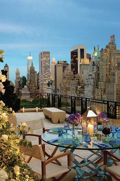 an outdoor dining table with candles and flowers on it in front of the city skyline