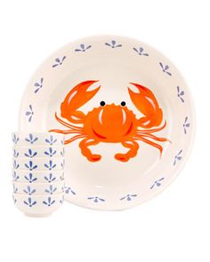 an orange crab on a white plate next to two blue and white dishes with matching cups