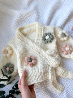 a hand is holding a sweater with flowers on it and the jacket has been knitted