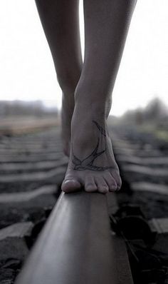 black and white photograph of a person's feet with tattoos on their ankles, walking along the pavement