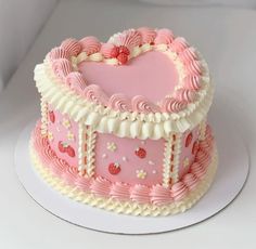 a pink heart shaped cake with white frosting and strawberrys on top, sitting on a plate