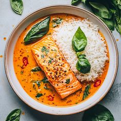 a bowl filled with fish and rice on top of a white table next to green leaves