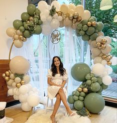 a woman sitting on a chair in front of an arch made out of balloons and greenery