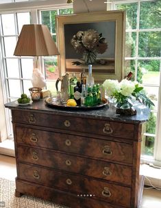 a chest of drawers in front of a window filled with wine bottles and other items