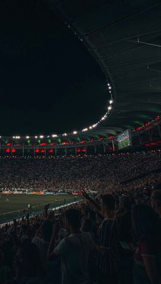 a stadium full of people at night with lights on the ceiling and fans in the stands