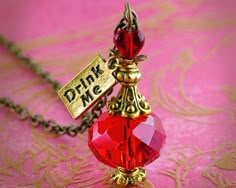 a red glass bottle with a gold chain attached to it that says drink me on the front