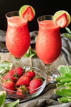 two glasses filled with strawberry margaritas next to strawberries and lime slices on a table