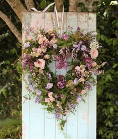 a heart shaped wreath hanging on the side of a wooden door with purple and pink flowers