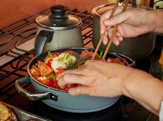 a person cooking food in a pot on top of the stove with chopsticks