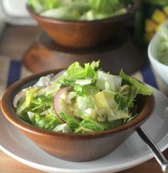 a salad with lettuce and onions in a wooden bowl on a white plate