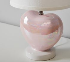 a pink heart shaped vase sitting on top of a table next to a white lamp