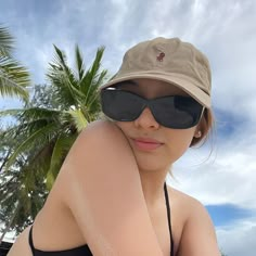 a woman wearing sunglasses and a hat sitting on the beach with palm trees in the background