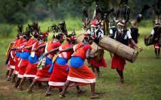 a group of people in red and blue outfits carrying wooden drums on their backs,