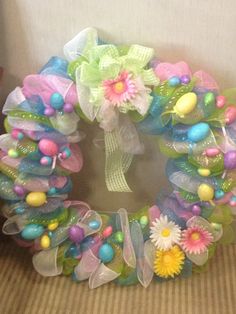 a colorful wreath with flowers and eggs on it sitting on a chair next to a wall