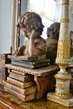 a statue of a child sitting on top of a pile of books next to a lamp