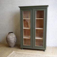 an armoire with two glass doors in front of a chair and rug on the floor