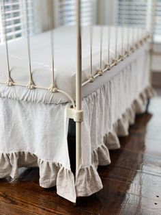 a white bed with ruffled bedspread and wooden floors