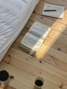 two cups of coffee and an open book on a wooden floor next to a bed