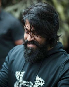 a man with long hair and a beard wearing a black hoodie looking at his cell phone