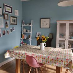 a dining room with blue walls and pictures on the wall, table covered in a floral print