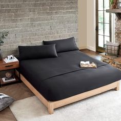 a bed with black sheets and pillows next to a brick wall