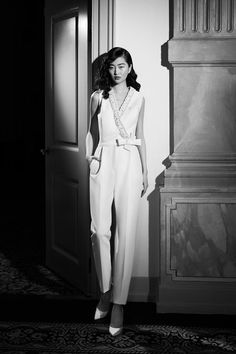 a woman standing in front of an open door wearing a white jumpsuit and heels