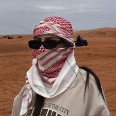 a woman wearing sunglasses and a red and white scarf on her head in the desert