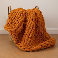 an orange knitted blanket sitting on top of a wooden floor next to a basket