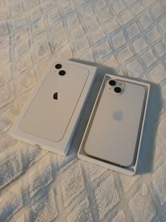 two white iphones sitting on top of a bed next to each other in a box